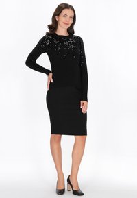 Fekete pulóver flitteres felsőrésszel és hosszú ujjakkal, fekete, testhez álló ceruzaszoknyával és fekete magassarkú cipőkkel párosítva.