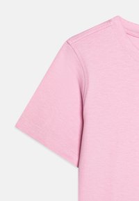 Detaliu despre un tricou roz din bumbac, prezentând mâneci scurte, un guler rotund și un material texturat cu cusături vizibile.