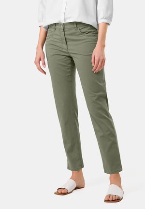 Olivgrüne, schmal geschnittene Hose mit fünf Taschen, Gürtelschlaufen und einem glatten, baumwollreichen Stoff. Kombiniert mit weißen Rutschen-Sandalen.