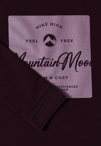 Felpa viola con un design grafico quadrato che presenta testo, montagne e polsini a costine. Texture morbida, stile casual e vestibilità comoda.