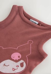 Haut sans manches côtelé rose poudré avec un visage de dessin animé portant un chapeau de bouffon avec un motif de crâne rose près de l'encolure.