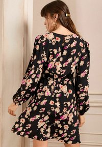 Rochie neagră cu motive florale, cu mâneci lungi și bufante, talie elastică și un amestec de modele roz deschis, crem și mov pe un material moale.