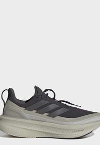 Μαύρο και γκρι παπούτσι για τρέξιμο Adidas Ultraboost με παχύ πέλμα Light Boost και θηλιά έλξης στη φτέρνα, εμφανίζεται από το πλάι σε απλό φόντο.