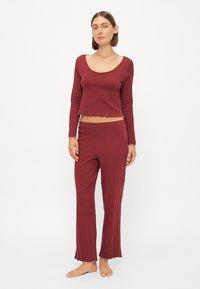 Burgundy lounge set bestående av en kortärmad topp med långa ärmar och utsvängda byxor, med ribbat mönster och vågiga kantdetaljer.