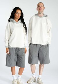 Hvide hættetrøjer med grå accenter, parret med løstsiddende grå shorts. Neoprenlignende tekstur, simpel design, ingen mønstre.