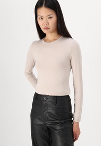 Licht beige lange mouw top met een ronde halslijn, een aansluitend ontwerp en een zachte textuur, gecombineerd met hoge zwarte neplederen broek.