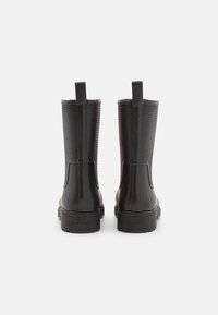 Botines negros con parte frontal lisa y parte trasera texturizada, con lengüetas para tirar y suela gruesa de goma.