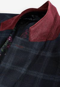 Mørkeblå ternet jakke med burgunder corduroy krave og blomsterpræget indvendig for, hvilket fremhæver teksturer og syningsdetaljer.