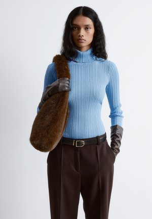 Helles blaues geripptes Rollkragenpullover, kombiniert mit braunen hoch taillierten Hosen. Das Model hält eine braune Felltasche und trägt dunkelbraune Handschuhe.
