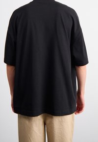 T-shirt in cotone nero con vestibilità ampia, maniche corte e orlo arrotondato. Design semplice, senza loghi o motivi visibili.