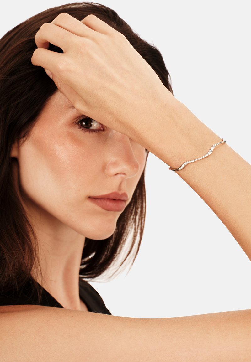 Bracciale in argento con un design ondulato e accenti trasparenti, caratterizzato da una texture liscia, indossato con eleganza su un polso.