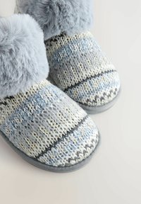 Pilkos megztos šlepetės su kailio apvadu, puoštos mėlynomis, pilkomis ir baltomis raštais, tekstūruota medžiaga ir kontrastinga tamsi padais.