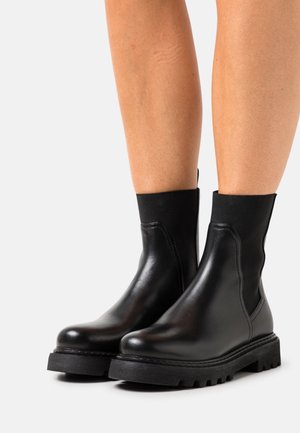 Botas de cuero negro hasta el tobillo con paneles laterales elásticos, puntera redondeada y suela de goma negra texturizada con profundas estrías para un buen agarre.