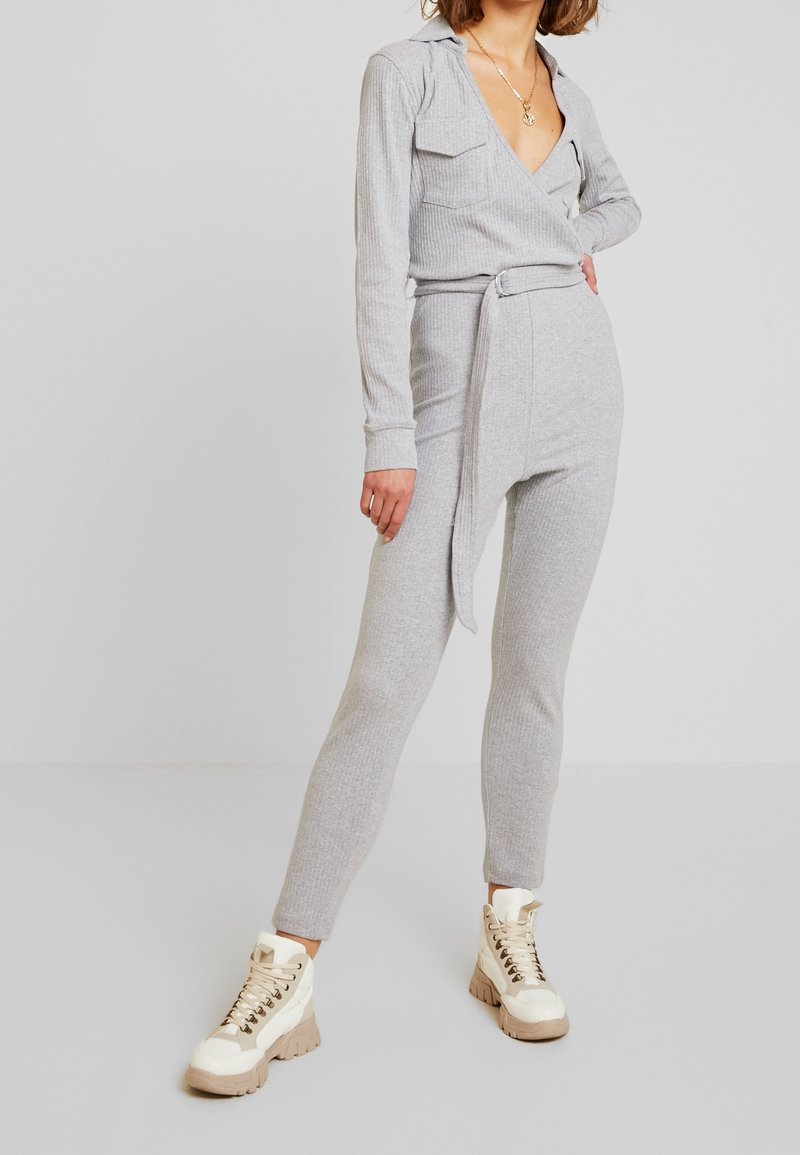 Salopette grise à côtes avec manches longues, col, deux poches avant, taille ceinturée et jambes fuselées, associée à des baskets montantes crème.