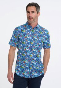 Korte mouwen shirt van blauwe stof met een levendig tropisch patroon met bladeren en bloemen in gele, rode en groene tinten.