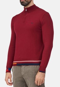 Maglione bordeaux a mezza zip, con maniche lunghe, colletto a coste e orlo a strisce con accenti arancioni, blu e navy.