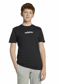 Melna kokvilnas t-kreklu ar īsām piedurknēm un apaļu kakla izgriezumu. Uz krūtīm ir baltais "adidas" logo. Saskaņots ar pelēkiem sporta biksēm.