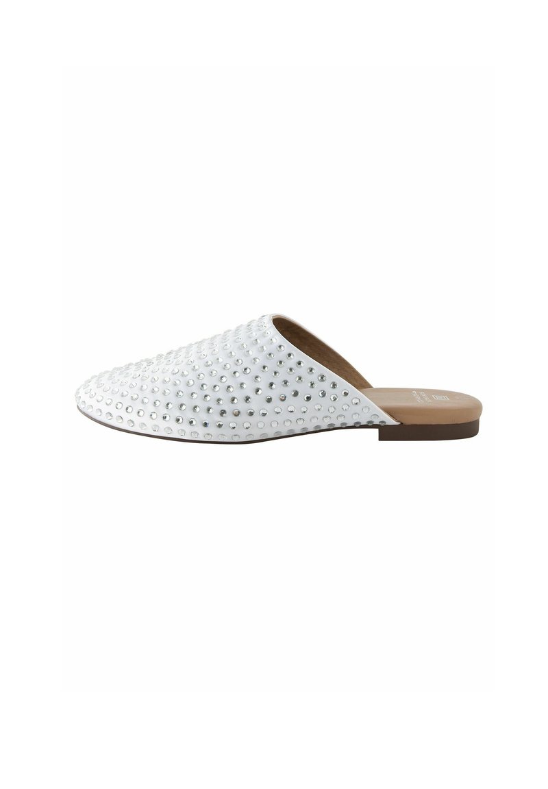 Vita slip-on sko med rund tå, prydd med silvernitar, slät textur och en platt, brun sula. Minimalistisk design för enkel användning.