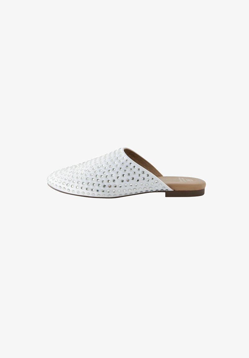 White slip-on shoe with rounded toe, adorned with silver studs, smooth texture, and a flat, brown sole. Minimalist design for ease of wear.