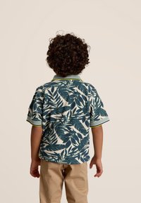 Korte mouwen shirt met een marineblauw en groen bladprint, voorzien van een kraag en gestreepte groene accenten. Gdrag met kaki broek.