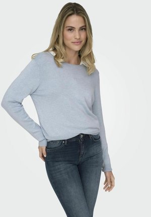 Pull à col rond bleu clair en tissu doux, porté avec un jean en denim foncé. Le pull a des manches longues et une coupe décontractée.