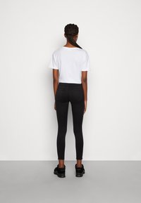 Calças de ganga skinny pretas com bolsos traseiros, combinadas com uma t-shirt branca de manga curta. O modelo está a usar ténis pretos e está de costas.