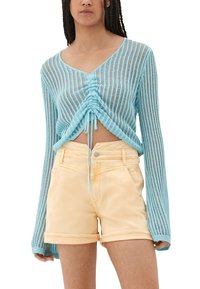 Hellblaues, langärmeliges Strickoberteil mit gerafftem Vorderteil und Bändern, kombiniert mit gelben Jeans-Shorts mit umgeschlagenen Säumen und Vorderentaschen.
