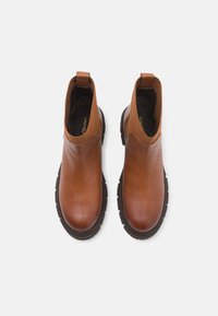 Bottines en cuir marron avec des panneaux élastiques sur les côtés, des languettes de tirage et des semelles en caoutchouc noir robustes, présentant une finition lisse et brillante.