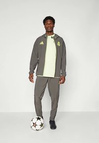 Harmaa urheilupuku neonkeltaisilla yksityiskohdilla. Sisältää vetoketjullisen takin ja siihen sopivat housut. Mukana mustat tennarit ja jalkapallo.