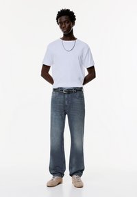 Vit kortärmad t-shirt, ljusblå raka jeans, svart nitarbält, beige sneakers, med ett enkelt silverhalsband.