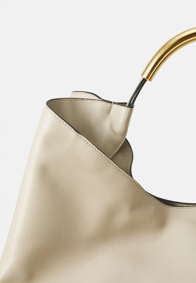 Sac à main en cuir beige avec une texture lisse et une anse en métal doré incurvée sur fond blanc uni.