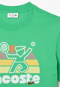 Camiseta de algodón verde con una gráfica de un jugador de tenis, con un logo debajo y rayas de atardecer estilizadas en tonos de amarillo, naranja y gris.