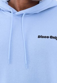 Felpa con cappuccio azzurro chiaro in tessuto morbido, con tasca frontale, coulisse e logo nero "Disco Only" stampato sul petto.