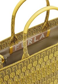 Bolso amarillo con tela negra de patrón intrincado, asas de cuero amarillo suave y un interior beige que incluye un bolsillo con cremallera y un logotipo.