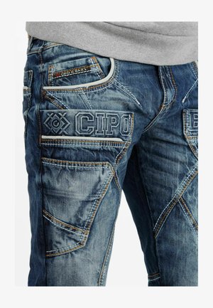 Blauwe denim jeans met meerdere zakken, ingewikkelde stiksels en geborduurd merk op de voorkant. Geverfd stof met een versleten uitstraling.