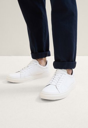Weiße Leder-Sneaker mit glatter Oberfläche, Schnürdesign und strukturiertem Gummisohle. Kombiniert mit hochgekrempelten blauen Hosen.