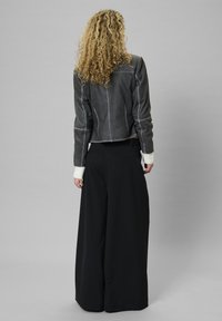 Szürke bőr, rövidített dzseki fehér mandzsetta részletekkel, fekete, bő szárú nadrággal párosítva. Simább textúra és letisztult dizájn.