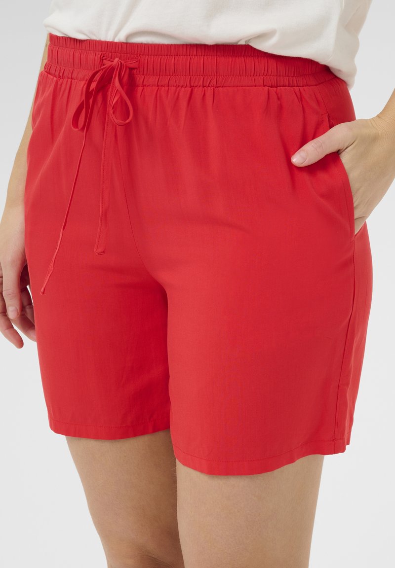 Röda shorts tillverkade av lättviktigt material, med elastiskt midjeband och dragsko, samt sidfickor för extra bekvämlighet.