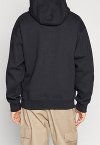 Czarny oversize hoodie z przednią kieszenią, z kapturem ze sznurkiem i ściągaczami na rękawach. Miękka tkanina i luźny krój podkreślają komfort noszenia.