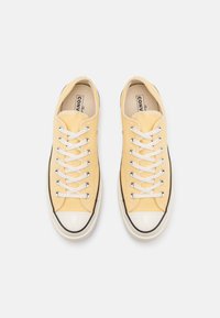 Baskets en toile jaunes avec lacets blancs, bout rond et semelle en caoutchouc noir. Présente des œillets en métal et une surface supérieure texturée.