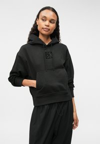 Μαύρη φούτερ μπλούζα με κουκούλα και μπροστινή τσέπη, διαθέτει λογότυπο στο στήθος και άνετη εφαρμογή. Μαλακό ύφασμα με ριμπ μανσέτες και στρίφωμα.