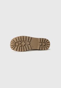 Suela de goma marrón con profundas suelas y patrones en forma de cruz diseñados para mejorar la tracción en el calzado.