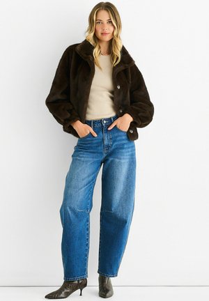 Brown faux fur jacket with a collar, button closure, and puffed sleeves, paired with light blue high-waisted jeans and patterned high-heel boots.
