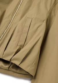Chaqueta caqui con una textura suave, que presenta un cierre metálico y un bolsillo lateral. El diseño incluye tela fruncida en el dobladillo.