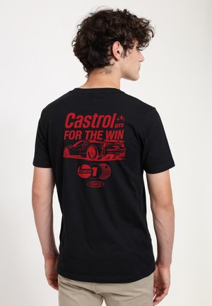 Giovane con capelli ricci che indossa una maglietta nera con una grafica rossa di un'auto da corsa e il testo "Castrol GTX For The Win" sul retro.
