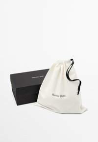 Scatola rettangolare nera e sacchetto bianco con coulisse con il marchio "Massimo Dutti" su uno sfondo bianco.