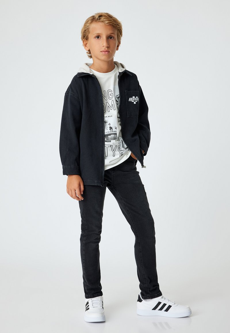 Chaqueta de mezclilla negra con sudadera gris debajo, camiseta gráfica blanca, jeans negros y zapatillas blancas con rayas negras. Diseño simple.