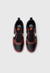 Nike-sko med en blanding av svarte, røde og hvite materialer, med perforert tå, svarte snøringer og en oransje logo-accent.