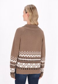 Taupe gebreide trui met een grote kraag, voorzien van een wit en zwart geometrisch patroon langs de onderrand. Zachte textuur, ontspannen pasvorm.