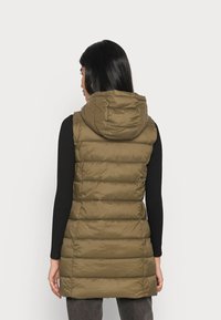 Olivgrön vadderad väst med huva, med vertikala quiltade paneler och åtsittande midja. Texturerad tyg ger en lätt glänsande finish.